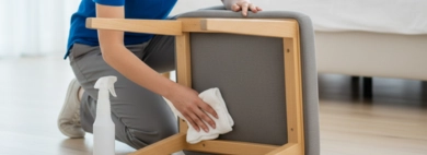 A close-up, detailed shot of a professional cleaner lifting and inspecting the underside of a wooden bedroom chair, carefully wiping the legs and frame to Clean Bottoms of Chairs, ensuring no dust or grime remains.