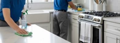 Professional team performing thorough Kitchen, with one person wiping down sparkling white countertops and another cleaning the sink and stove area in a modern kitchen.