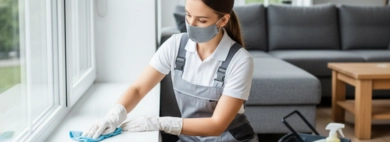 A professional cleaner, wearing gloves and a mask, meticulously wiping down a spotless windowsill in a bright living room, demonstrating thorough Wipe Windowsills Cleaning services.