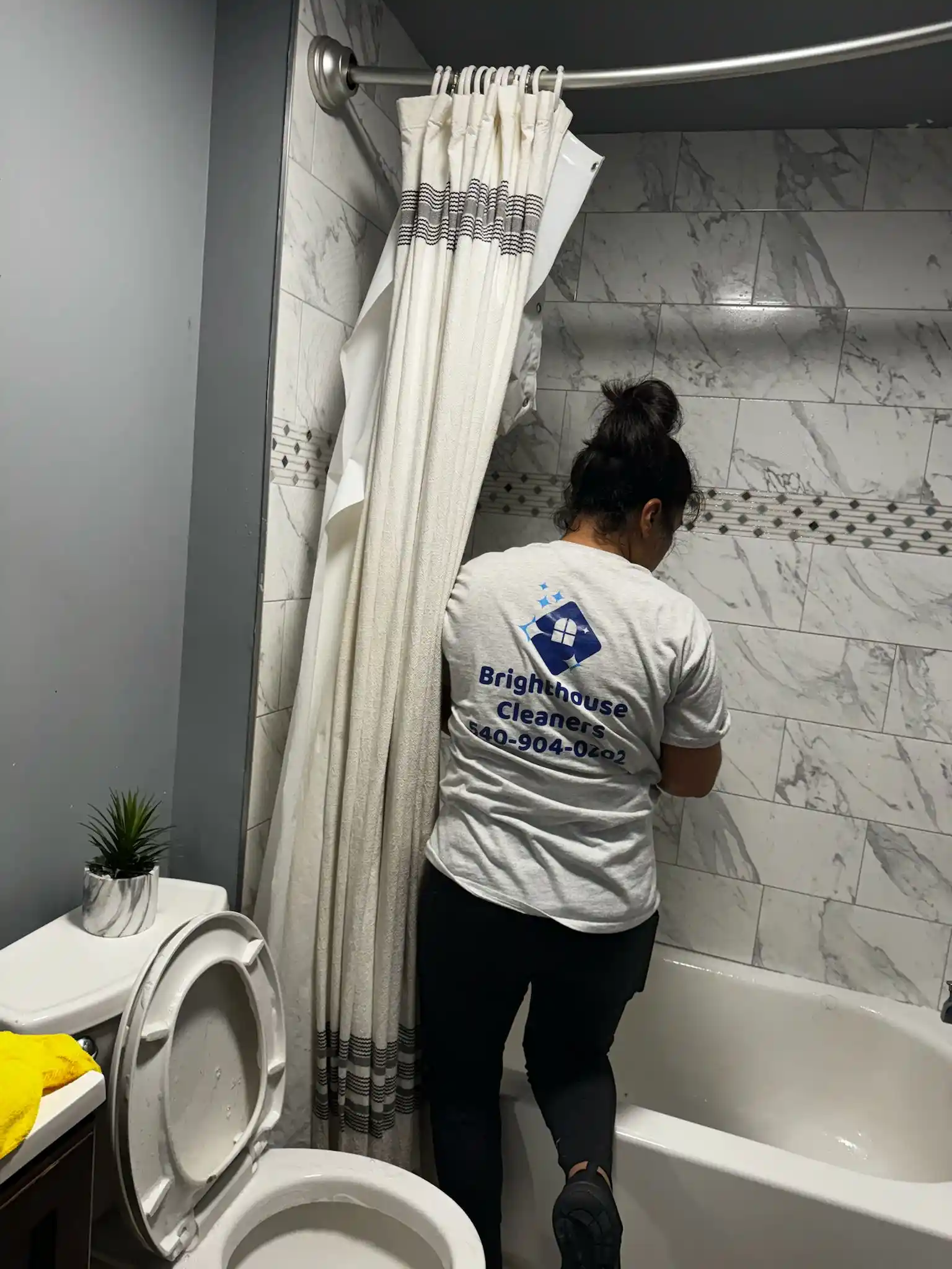 A Brighthouse Cleaners provides a detailed bathroom cleaning service, seen cleaning a modern, marble-tiled shower.