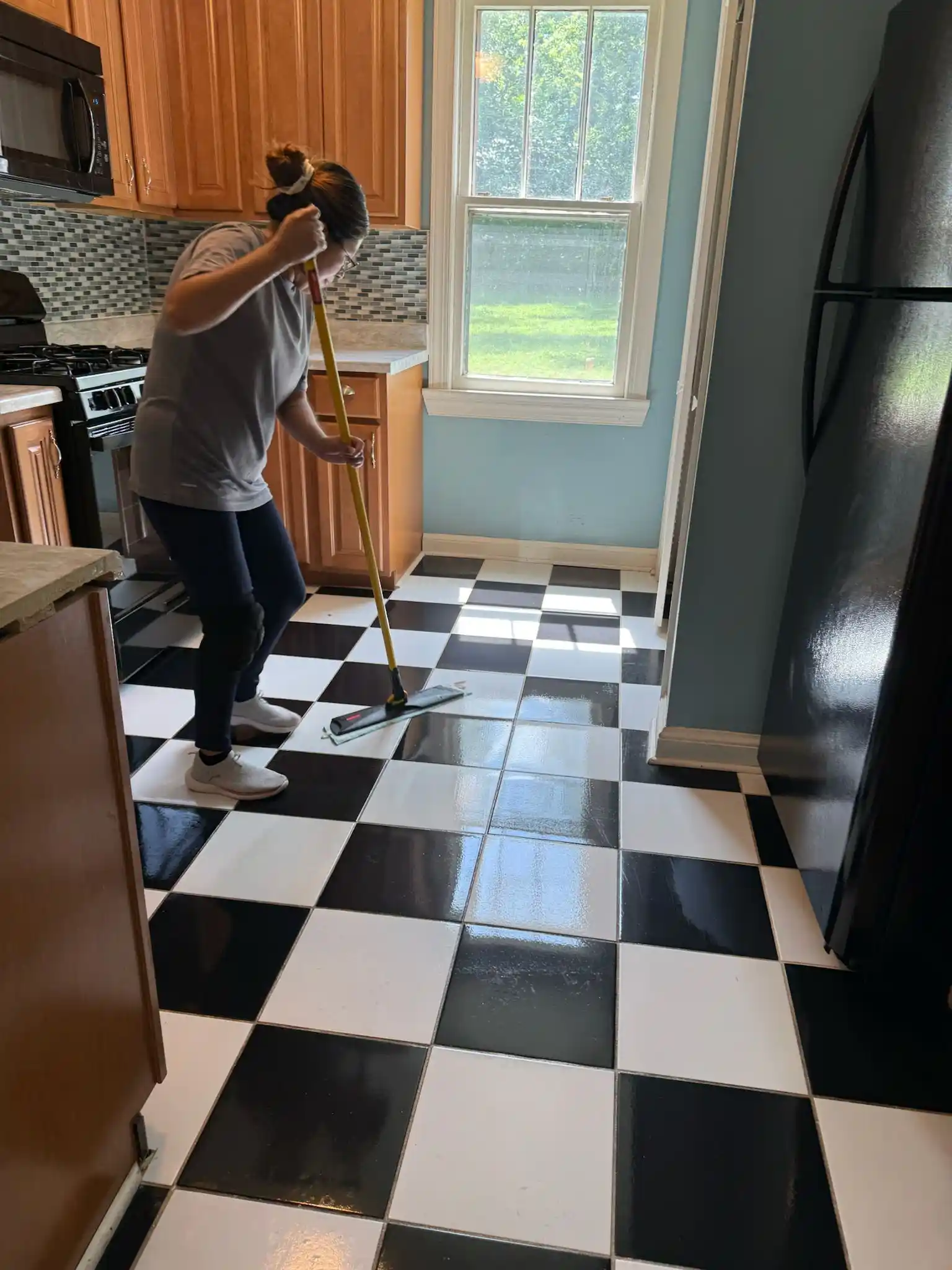 A Brighthouse Cleaners professional performing a post-construction cleaning service by meticulously mopping a black and white checkered kitchen floor.